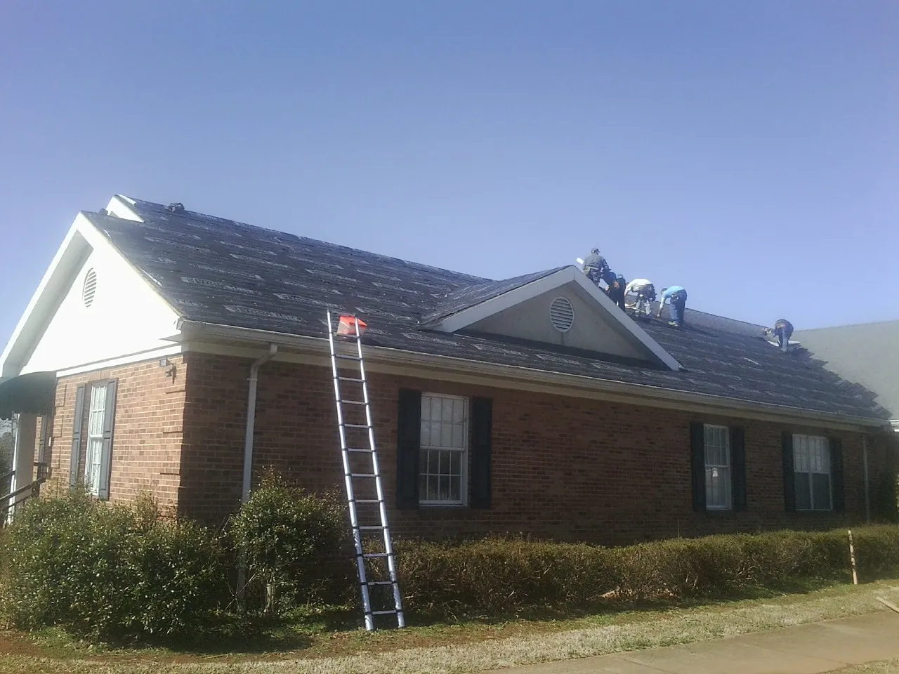 Crew tearing shingles off a brick ranch roof with a ladder set — Emergency Roof Repair work by our crew in Kenansville
