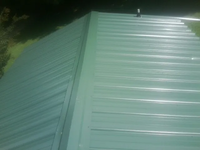 New green metal panels meeting at the ridge of a roof — Flat Roof Repair work by our crew in Kenansville