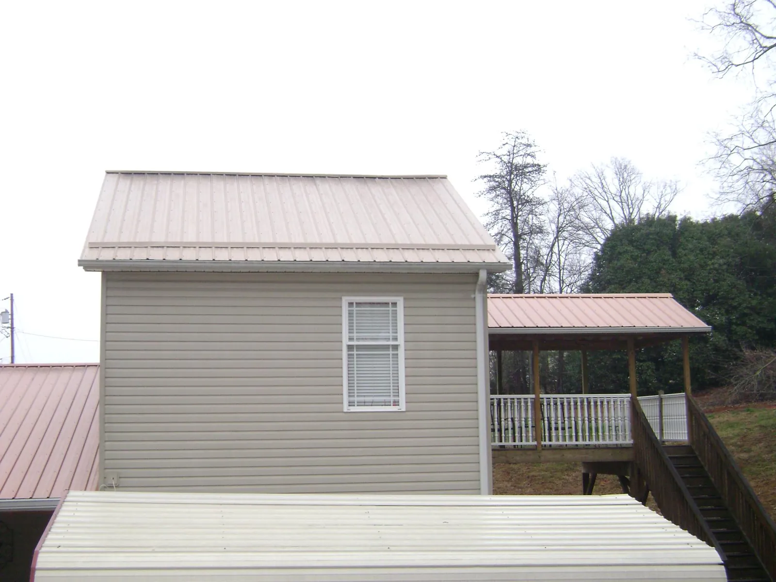 Tan metal roofs on a two story addition and attached porch, from a Roof Replacement job in Kenansville